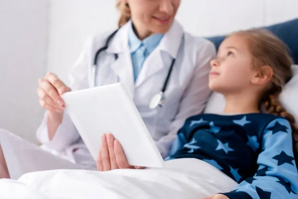 Селективный фокус врача в белом халате, держащего цифровой планшет рядом с больным ребенком — стоковое фото