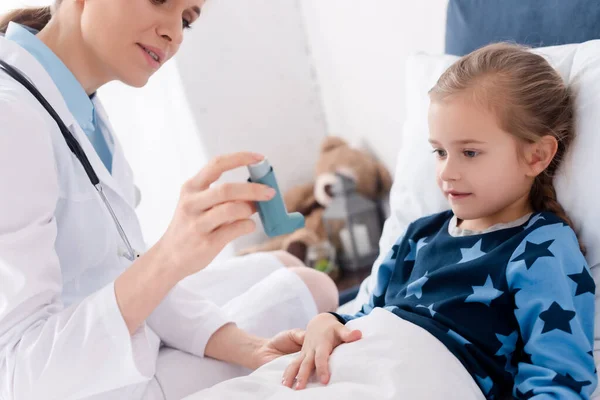 Doctor in white coat holding inhaler near asthmatic child — Stock Photo