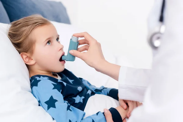 Foco seletivo do médico segurando inalador perto de criança asmática com boca aberta — Fotografia de Stock