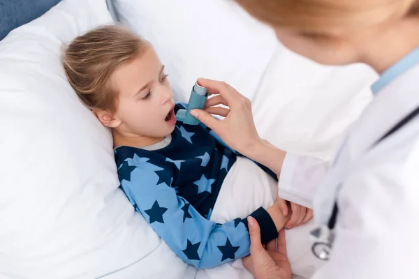 Selective focus of doctor holding inhaler near asthmatic kid with opened mouth — Stock Photo