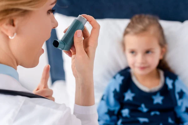 Селективний фокус привабливого лікаря з відкритим ротом, що тримає інгалятор біля астми дитини — стокове фото