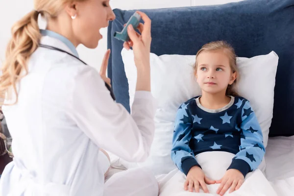 Messa a fuoco selettiva del bambino asmatico guardando medico attraente con bocca aperta che tiene inalatore — Foto stock