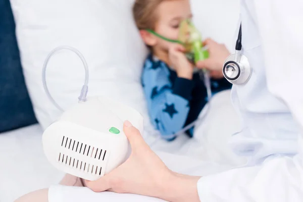 Selective focus of doctor holding compressor inhaler near sick kid — Stock Photo