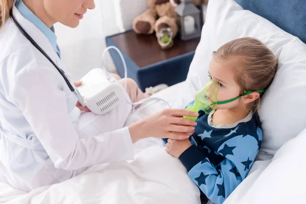 Médecin en manteau blanc touchant masque respiratoire sur enfant asthmatique en utilisant un inhalateur compresseur — Photo de stock