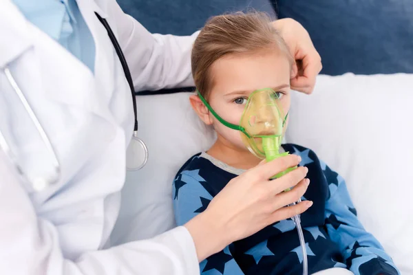 Médico de bata blanca tocando máscara respiratoria en niño asmático - foto de stock