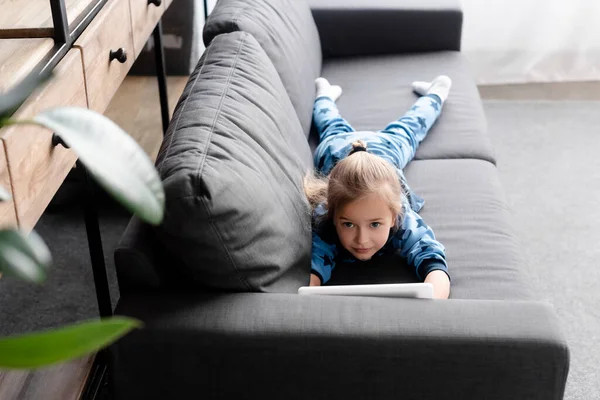 Selective focus of cute kid using digital tablet while lying on sofa — Stock Photo