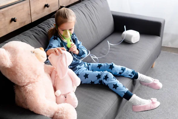 Asthmatic kid using compressor inhaler near soft toys — Stock Photo