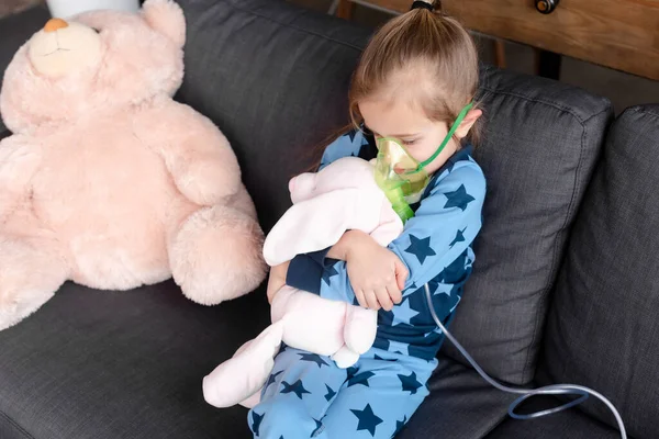 Niño asmático usando máscara respiratoria mientras abraza juguete suave - foto de stock
