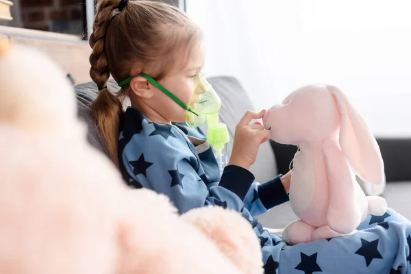 Foco seletivo da criança asmática usando máscara respiratória e brincando com brinquedo macio — Fotografia de Stock