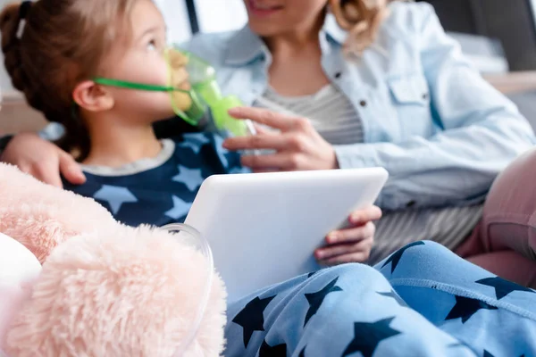 Selektiver Fokus asthmatischer Kinder mit Atemmaske und digitalem Tablet in der Nähe von Mutter und Plüschtier — Stockfoto