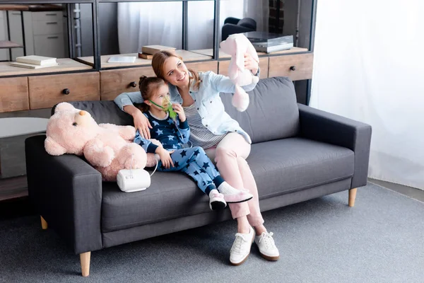 Asthmatic kid using compressor inhaler near mother with soft toy — Stock Photo