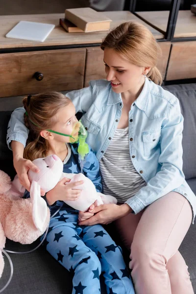Enfoque selectivo de niño asmático usando máscara respiratoria y mirando juguete suave cerca de la madre - foto de stock