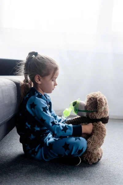 Vista laterale del bambino carino che tiene orsacchiotto in maschera respiratoria — Foto stock