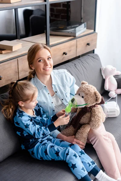 Bambino guardando maschera respiratoria su orsacchiotto vicino alla madre felice — Foto stock