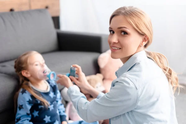 Fuoco selettivo della madre che tiene l'inalatore con distanziatore vicino al bambino — Foto stock