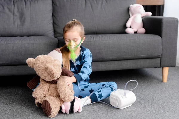 Asthmatic child using compressor inhaler and holding teddy bear — Stock Photo