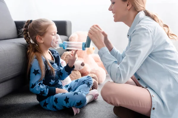 Felice madre che tiene l'inalatore con distanziatore vicino al bambino malato — Foto stock