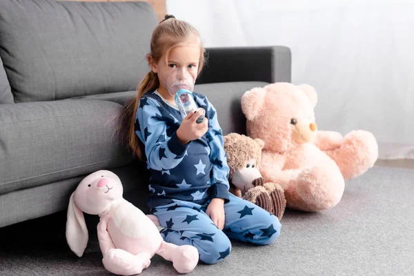 Enfant asthmatique en utilisant un inhalateur avec espaceur près de jouets mous — Photo de stock