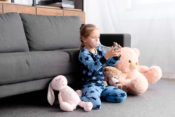 Diseased kid using inhaler with spacer near soft toys — Stock Photo