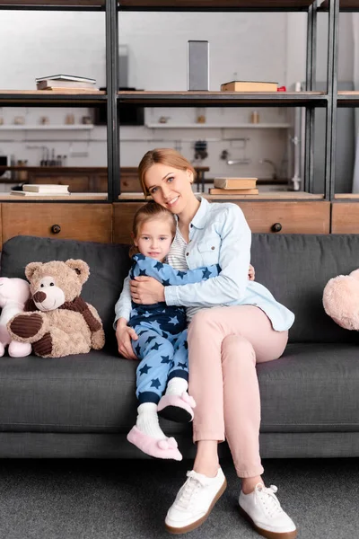 Bonito criança abraçando mãe perto de brinquedos macios no sofá — Fotografia de Stock