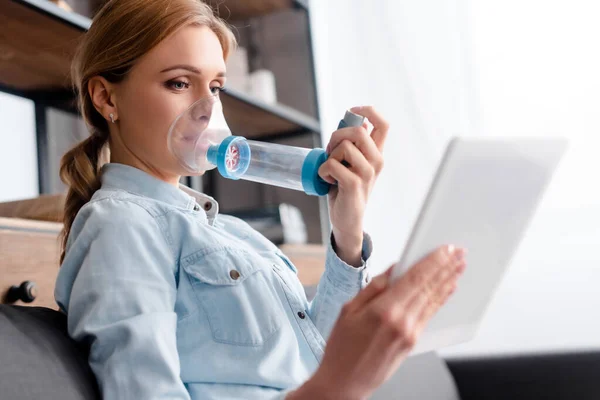 Enfoque selectivo de la mujer enferma usando inhalador con espaciador y sosteniendo tableta digital - foto de stock