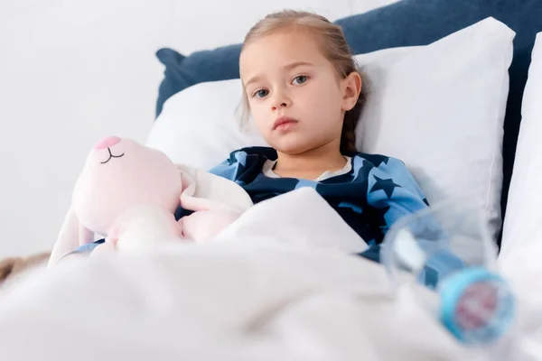 Selective focus of sick kid near inhaler with spacer and bunny toy — Stock Photo