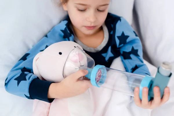 Selective focus of sick kid holding inhaler with spacer near bunny toy — Stock Photo