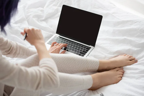 Vista recortada do freelancer com caneta trabalhando no laptop na cama — Fotografia de Stock