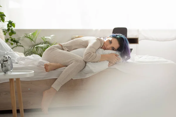 Вибірковий фокус красивої дівчини з барвистим волоссям, що лежить на ліжку і дивиться на камеру в спальні — стокове фото