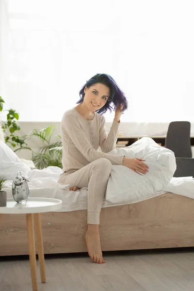 Belle femme aux cheveux colorés regardant la caméra et souriant sur le lit dans la chambre — Photo de stock