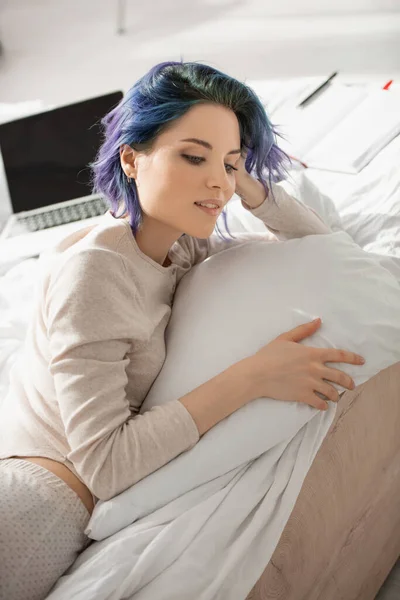 Dreamy freelancer with colorful hair lying near laptop on bed — Stock Photo