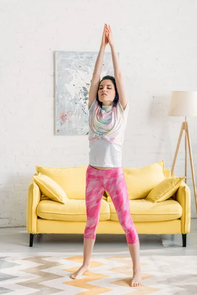 Mulher com cabelo colorido, mãos apertadas e olhos fechados fazendo ioga asana na sala de estar — Fotografia de Stock