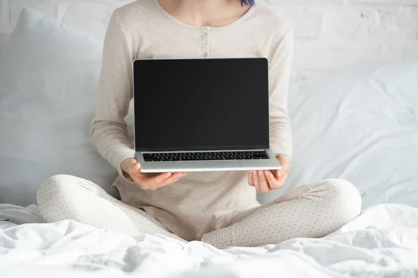 Cropped view of freelancer with colorful hair and crossed legs showing laptop on bed in bedroom — Stock Photo