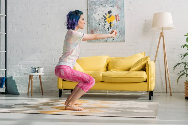 Chica con el pelo colorido en la silla pose con las manos extendidas en la sala de estar - foto de stock