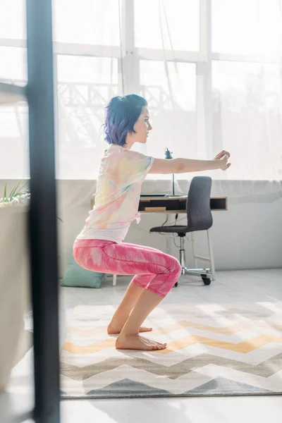 Selektiver Fokus des Mädchens mit buntem Haar, ausgestreckten und geballten Händen in Stuhlpose im Wohnzimmer — Stockfoto