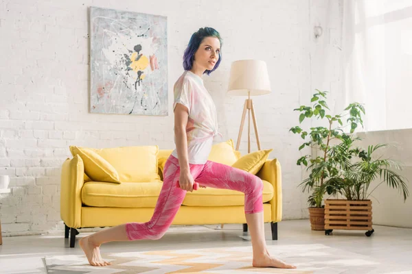 Beautiful girl with colorful hair doing lunges with dumbbell in living room — Stock Photo