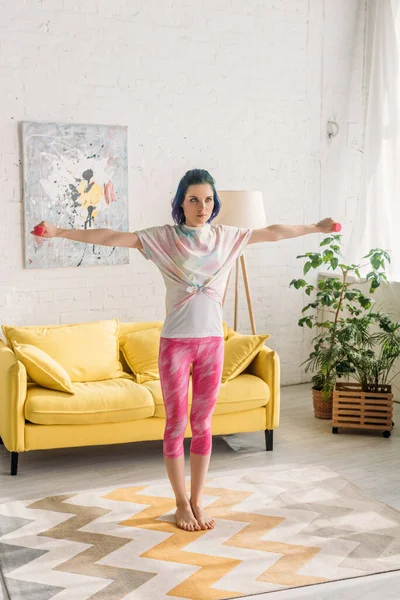 Tense woman with colorful hair holding dumbbells with outstretched hands in living room — Stock Photo