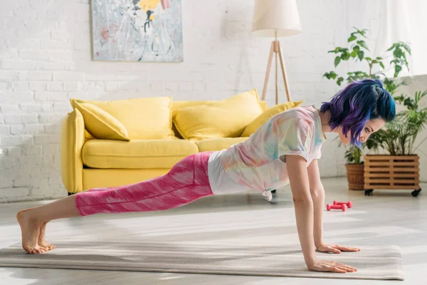 Woman with colorful hair doing plank on yoga mat in living room — Stock Photo