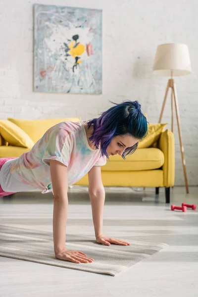 Konzentrierte Frau mit buntem Haar macht Planke auf Yogamatte im Wohnzimmer — Stockfoto
