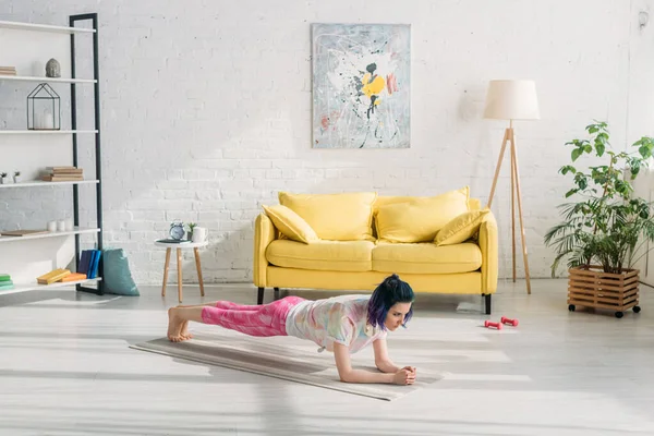 Mädchen mit bunten Haaren beim Planken auf Yogamatte neben Sofa im Wohnzimmer — Stockfoto