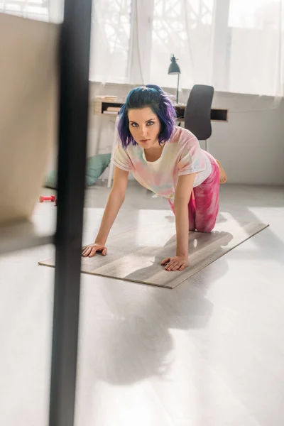 Concentration sélective de la fille avec des cheveux colorés sur tous les quatre sur tapis de fitness en regardant la caméra dans le salon — Photo de stock