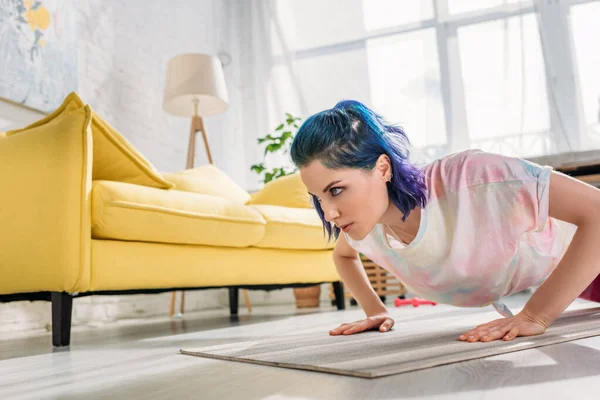Напряженная девушка с красочными волосами делает отжимания на фитнес-мат в гостиной — стоковое фото