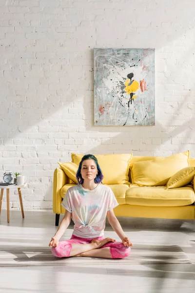 Girl with colorful hair and closed eyes meditating on yoga mat in living room — Stock Photo