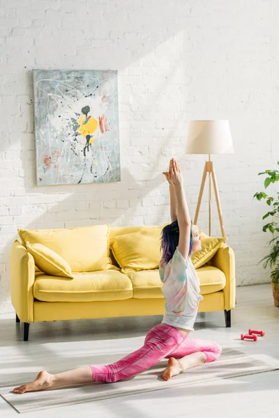 Femme aux cheveux colorés en pose de pigeon sur tapis de yoga dans le salon — Photo de stock