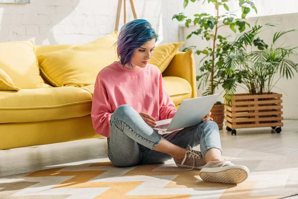 Freelancer with colorful hair working with laptop near sofa in living room — Stock Photo