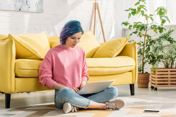Freelancer com cabelo colorido trabalhando com laptop perto de smartphone no chão — Fotografia de Stock