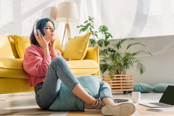 Freelancer in headphones with colorful hair and closed eyes near sofa on floor in living room — Stock Photo