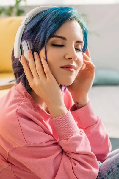 Hermosa mujer con cabello colorido y ojos cerrados en auriculares escuchando música y sonriendo - foto de stock