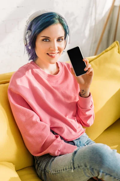 Weitwinkelbild einer Frau mit buntem Haar und Kopfhörern, die lächelt, in die Kamera blickt und ihr Smartphone zeigt — Stockfoto