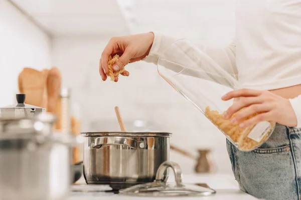 Cropped view of girl putting pasta in pan near kitchen stove — Stock Photo